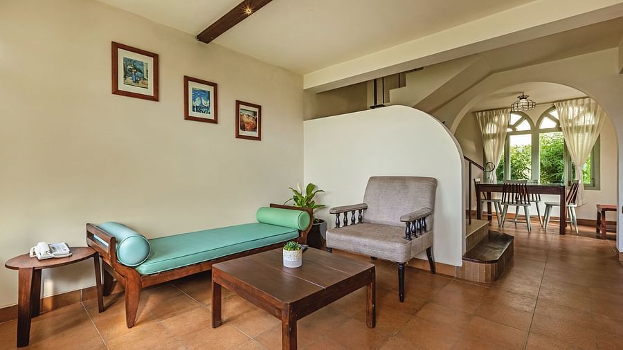 Living area at Mango Hill Shola, Ooty, with cushioned seating, a coffee table, and arched windows allowing in natural light.