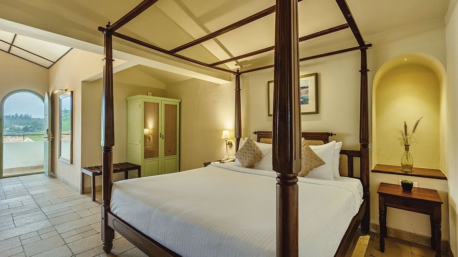 Charming bedroom at Mango Hill Shola, Ooty with an inviting four-poster bed and arched niche detail near the headboard.