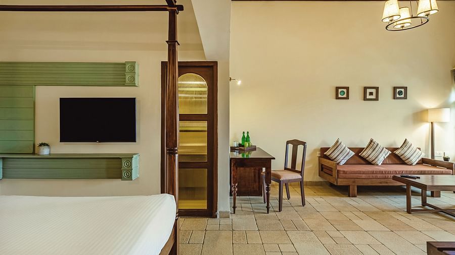 Deluxe Room at Mango Hill Shola, Ooty featuring a four-poster bed, mounted TV, writing desk, and a cosy lounge area with a cushioned wooden sofa and warm ambient lighting.