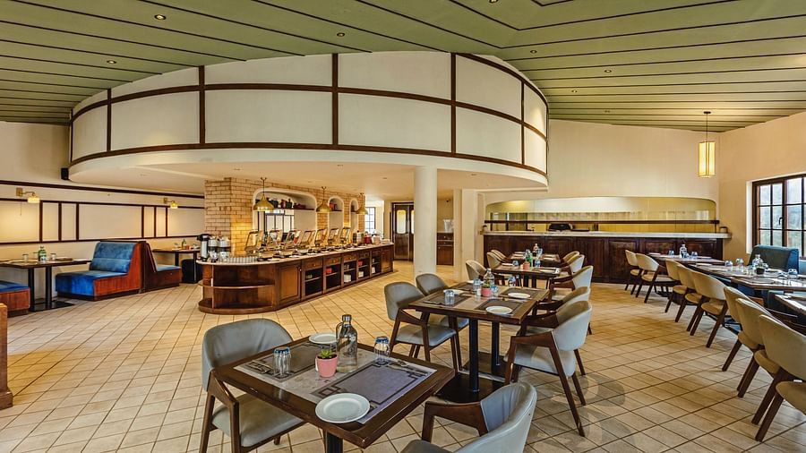 Spacious restaurant interior at Mango Hill Shola, Ooty, showcasing a curved buffet counter, comfortable booth seating, and wooden ceiling panels in a well-lit dining space.