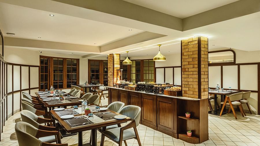 Stylish restaurant seating at Mango Hill Shola, Ooty with wood and glass accents, neutral tones, and thoughtfully arranged table settings.