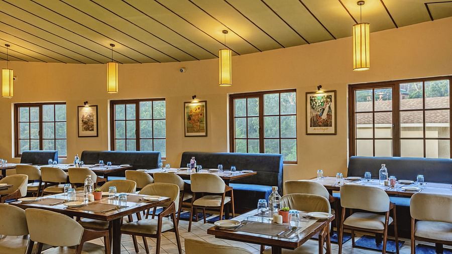 Cosy and well-lit dining space at Mango Hill Shola, Ooty with wooden ceiling accents and window-side tables arranged for a comfortable meal experience.