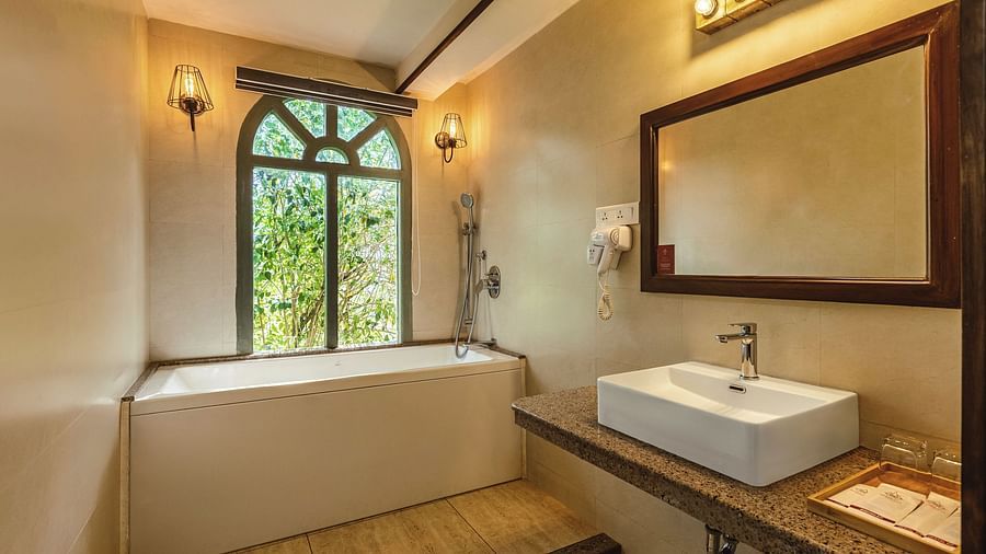 uxurious bathroom at Mango Hill Shola, Ooty featuring a deep soaking tub, wide mirror, and warm ambient lighting.