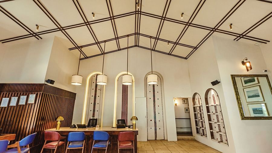 Elegant indoor dining space at Mango Hill Shola, Ooty, showcasing a large wooden table, varied seating, and overhead lights suspended from a high beamed ceiling.