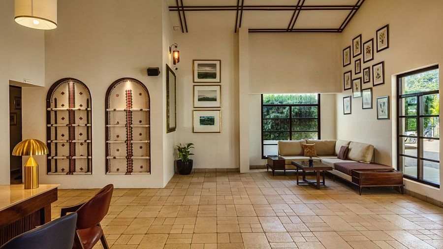 A side angle view of a welcoming indoor area at Mango Hill Shola, Ooty, with tiled flooring, cushioned seating, and expansive windows offering plenty of daylight.