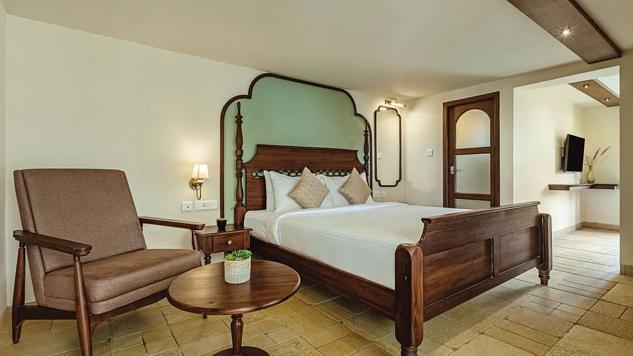 Charming bedroom at Mango Hill Shola, Ooty with classic wooden furniture, armchairs, and soft ambient lighting.