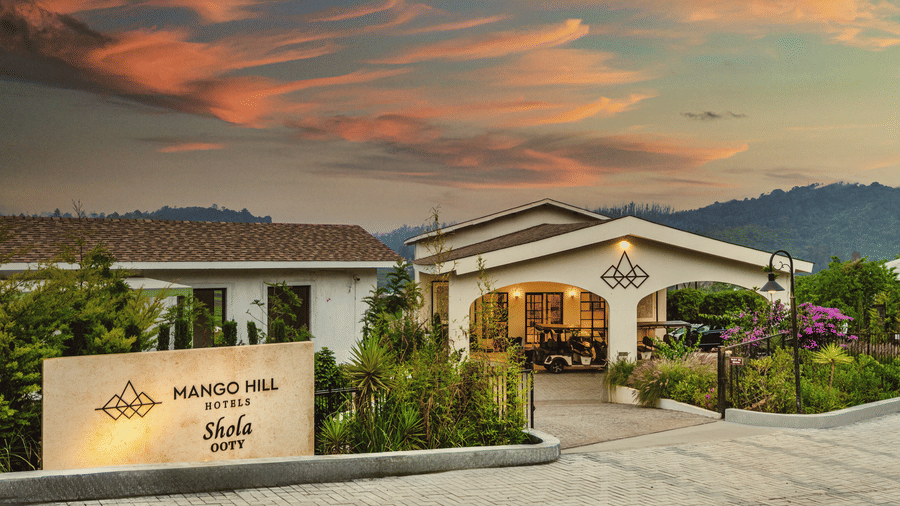Panoramic view of Mango Hill Shola, Ooty, nestled within tea plantations and hills, blending into the expansive surrounding landscape.