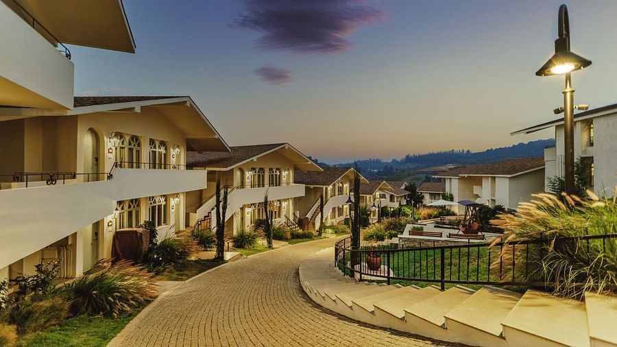 Distant view of a valley near Mango Hill Shola, Ooty, featuring gently sloping hills and scattered buildings.