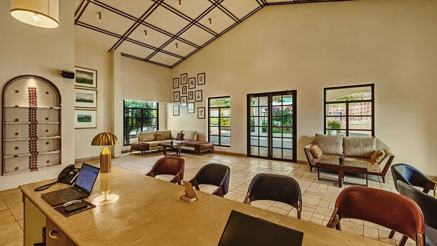 Interior view of a spacious dining area at Mango Hill Shola, Ooty, featuring a long wooden table with chairs, high ceilings with exposed beams, and large windows overlooking the surroundings.