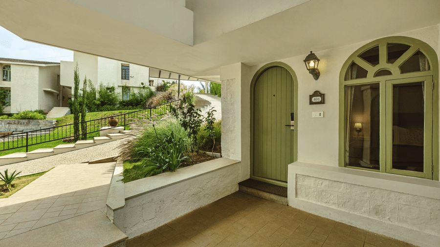 Exterior view of a cottage-style room entrance at Mango Hill Shola, Ooty with arched doors, stucco walls, and garden walkway.
