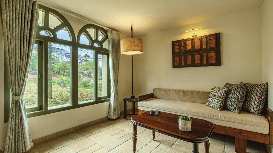 Corner view of a bright room at Mango Hill Shola, Ooty with full-length arched windows, natural light, and a daybed seating nook.