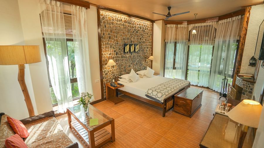 A bedroom with a bed, lamps, and a view of a garden - The Den Corbett Resort & Spa, Kumeria.