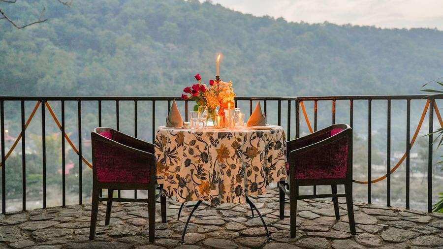 A patio with a table and chairs, decorated with flowers and candles, overlooking a valley with trees and mountains.
