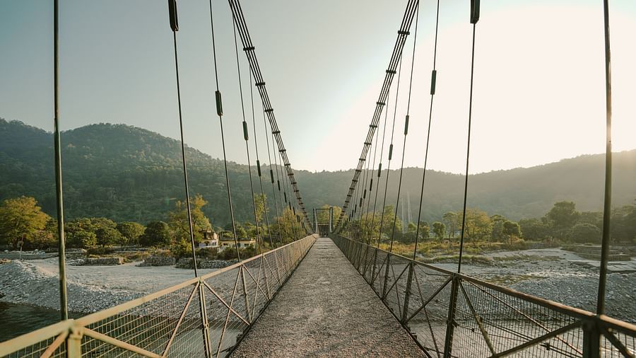 A suspension bridge over a river, with mountains in the background, daytime setting.