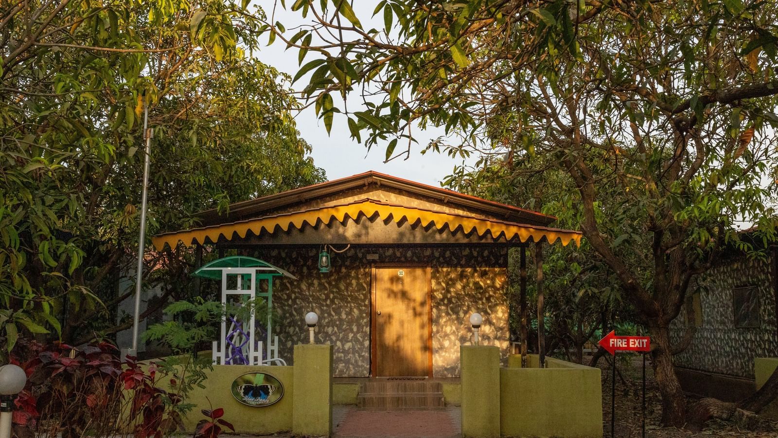 A small wooden hut with a green sign surrounded by trees, at Daksh Resort & Amusement Park, Sasan Gir.
