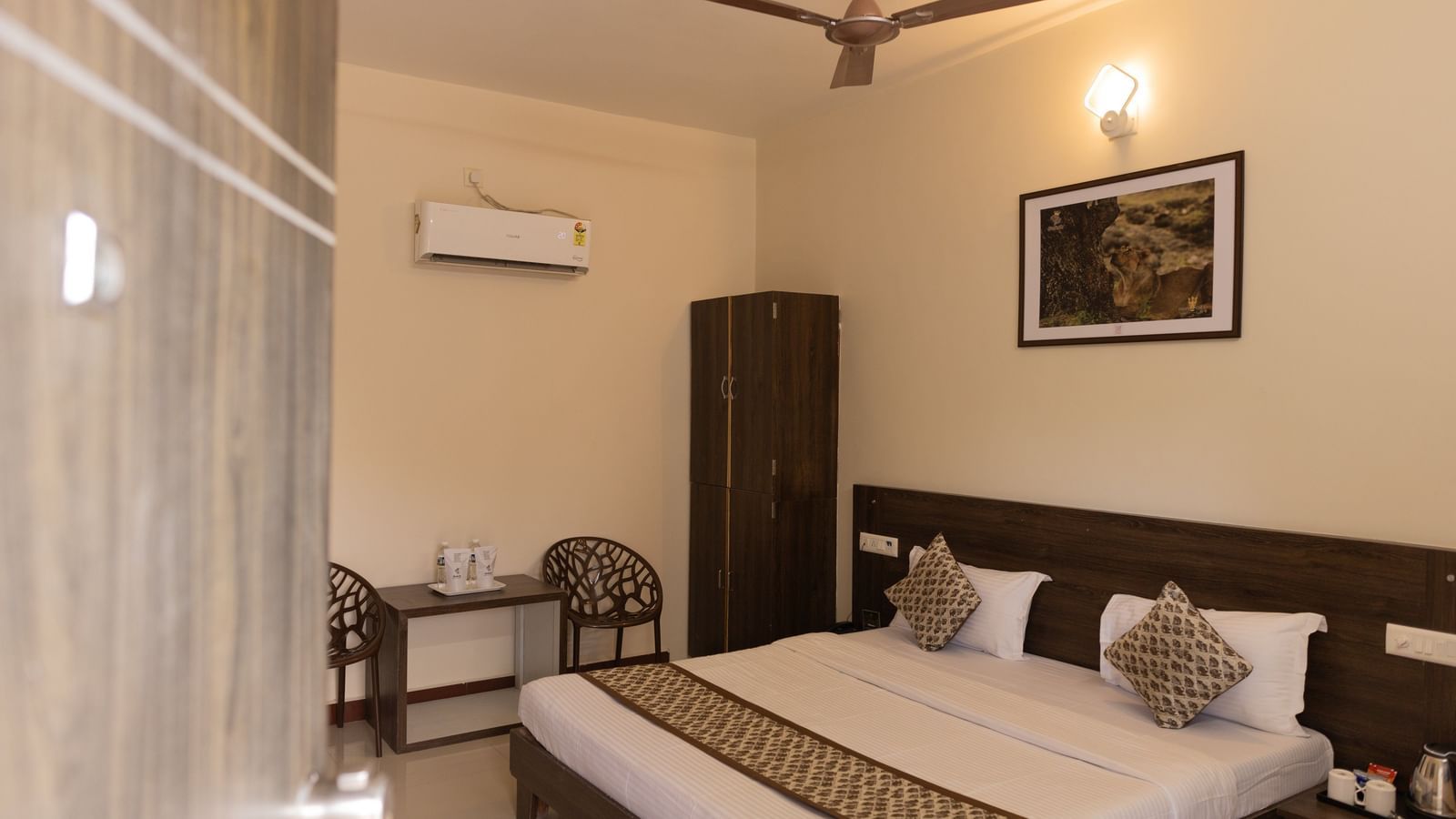 A room with a king size bed, a wall art, a wooden wardrobe and a table and chairs arranged neatly at Daksh Resort & Amusement Park, Sasan Gir.