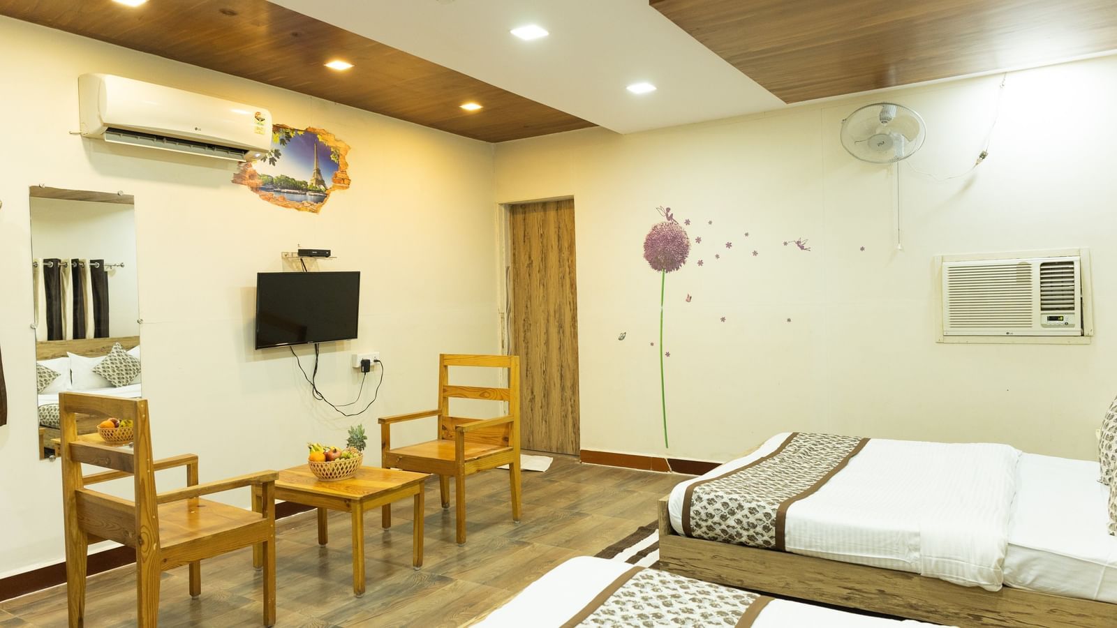 The interior of a room with 2 beds, a TV, and wooden chairs with a table at Daksh Resort & Amusement Park, Sasan Gir.