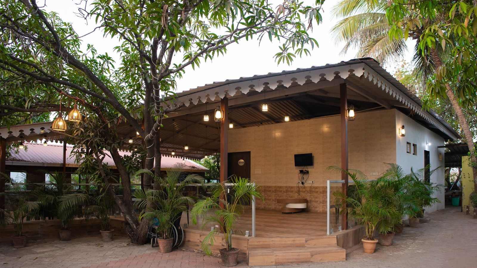 Exterior of Daksh Resort & Amusement Park surrounded by potted plants and trees, with a tiled path leading to the entrance.