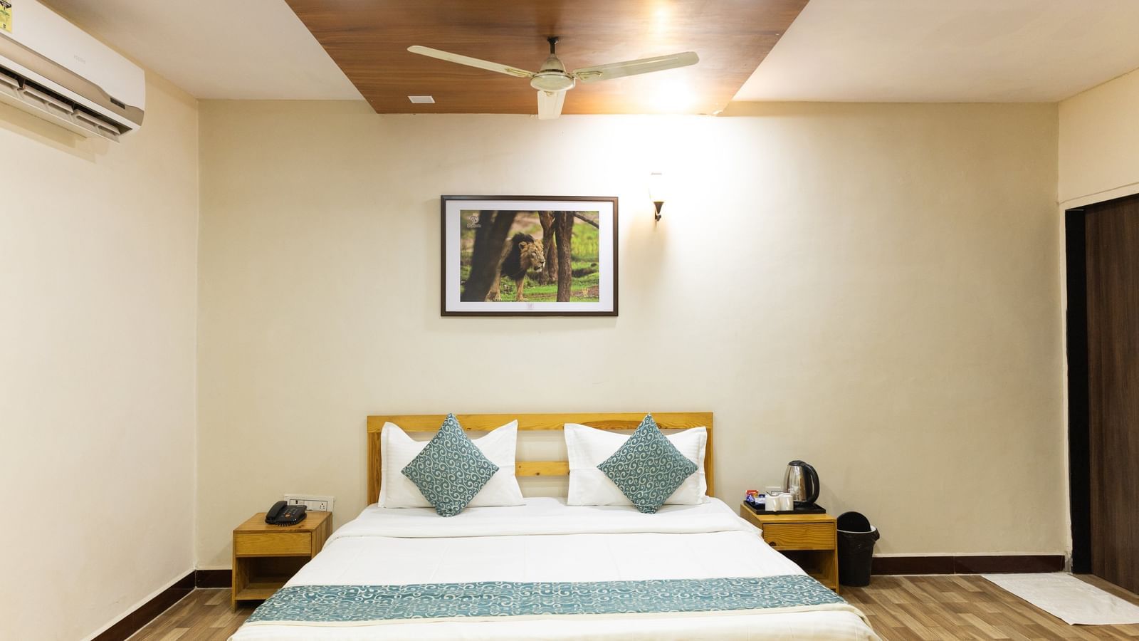 A room with a double bed, blue cushions and a runner, wall art, and ceiling fan at Daksh Resort & Amusement Park.