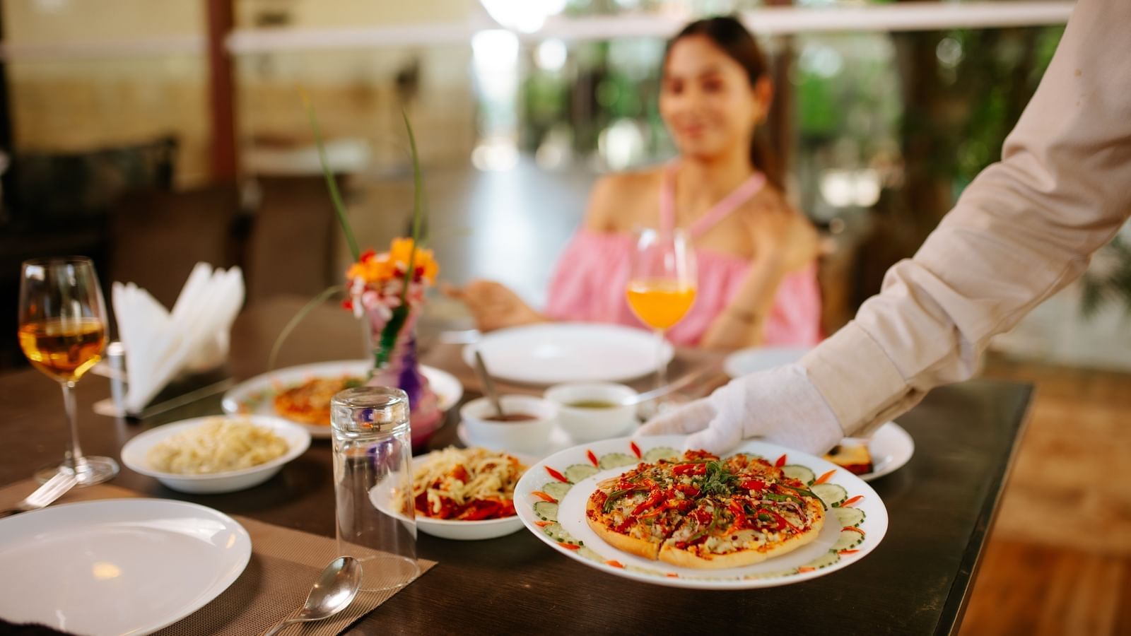 A waiter serving pasta and drinks at a restaurant table, with a woman seated and smiling at Daksh Resort & Amusement Park.