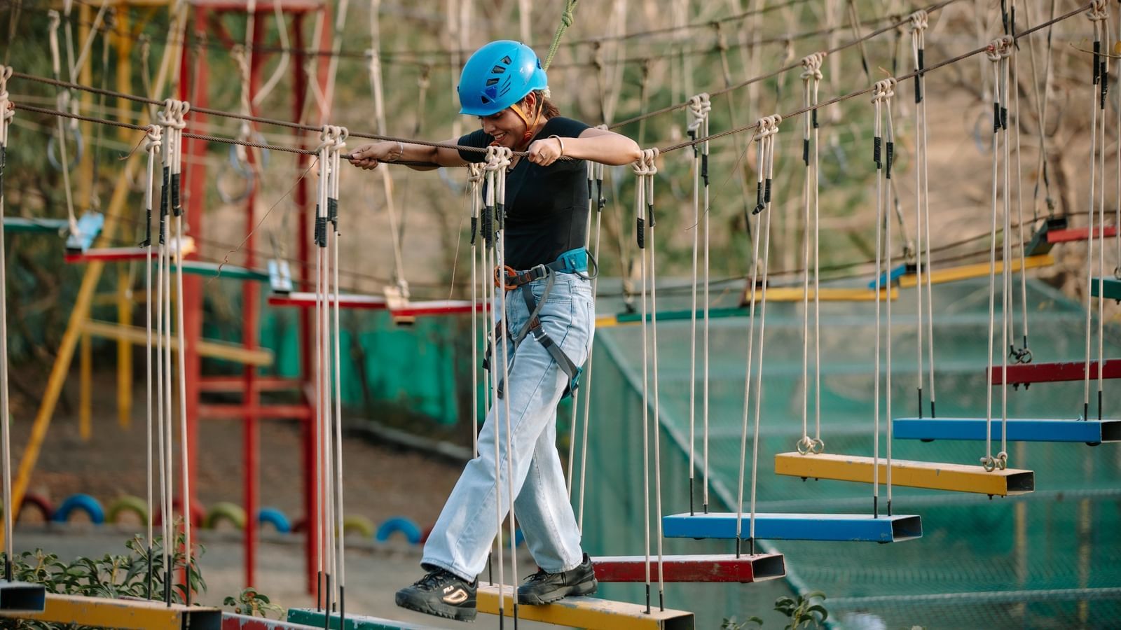 A person balancing on a rope bridge wearing safety gear and a helmet at Daksh Resort & Amusement Park.