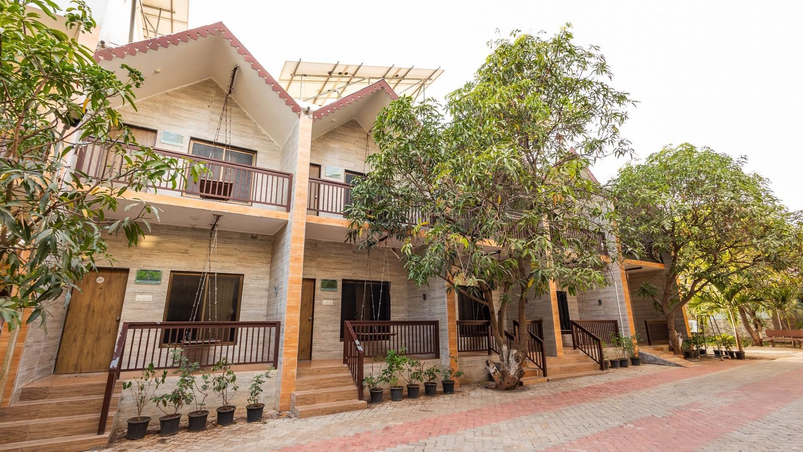 Exterior view of Daksh Resort & Amusement Part featuring a two-storey resort building with balconies, trees, and a paved driveway in the front.