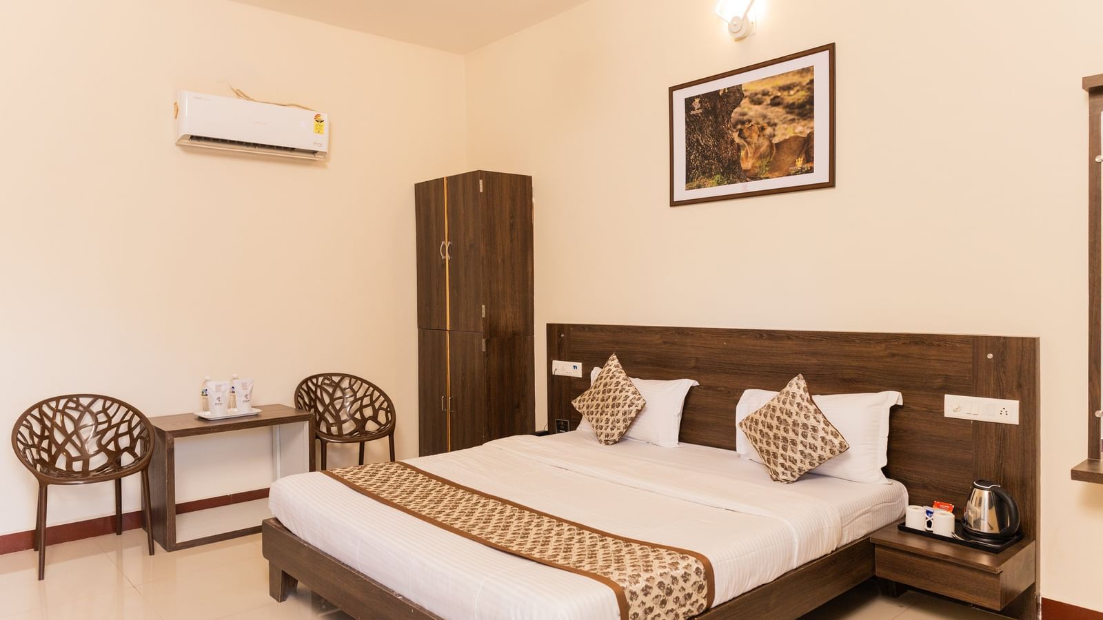 A double bed with patterned cushions, wall art, and chairs in a guest room at Daksh Resort & Amusement Park.