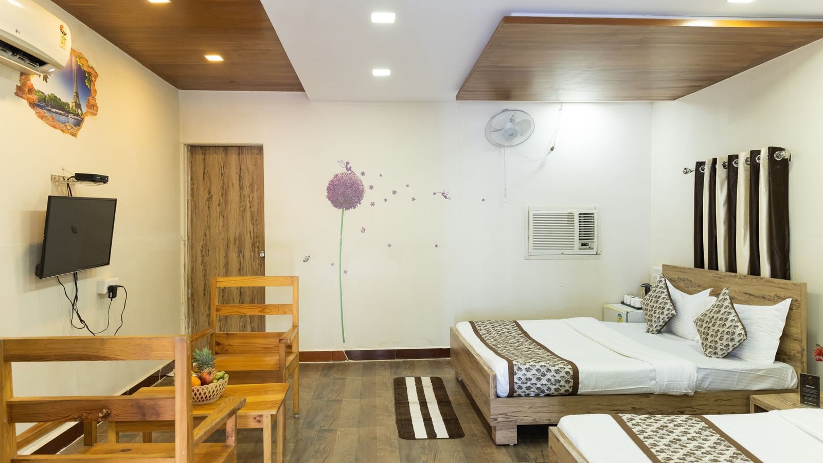 A guest room with beds, wooden chairs, a wall-mounted T.V., and striped rugs at Daksh Resort & Amusement Park.