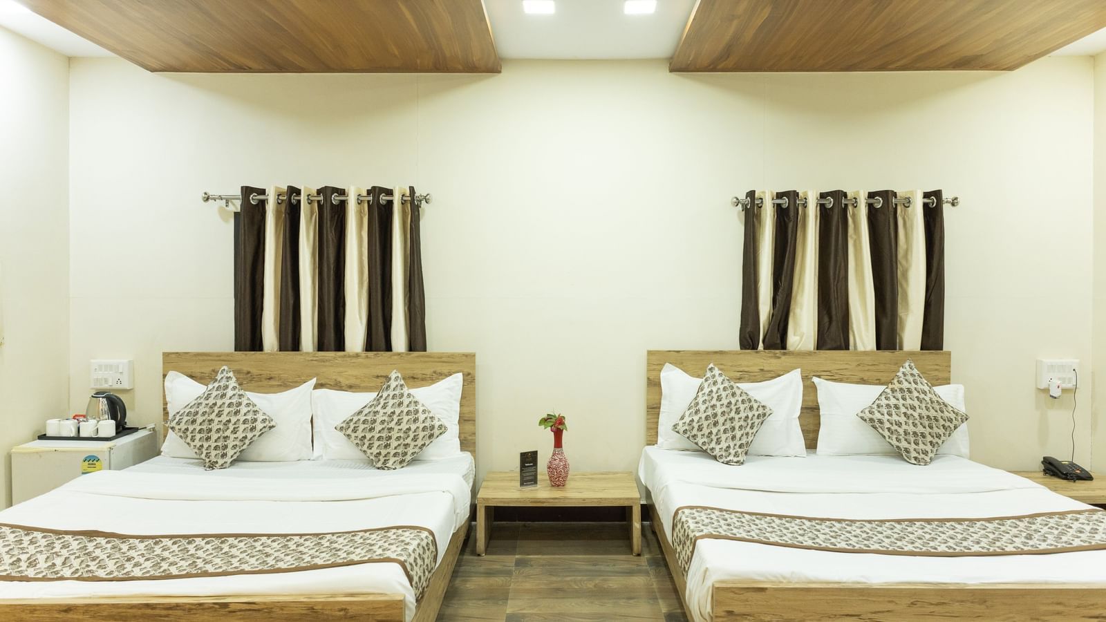 A guest room with two double beds, brown and white curtains, and ceiling lights at Daksh Resort & Amusement Park.