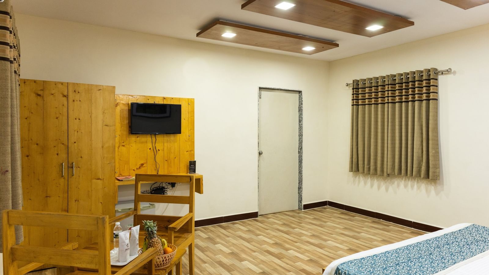 A guest room with a wooden wardrobe, wall-mounted T.V., a dining set with a partially visible bed at Daksh Resort & Amusement Park.