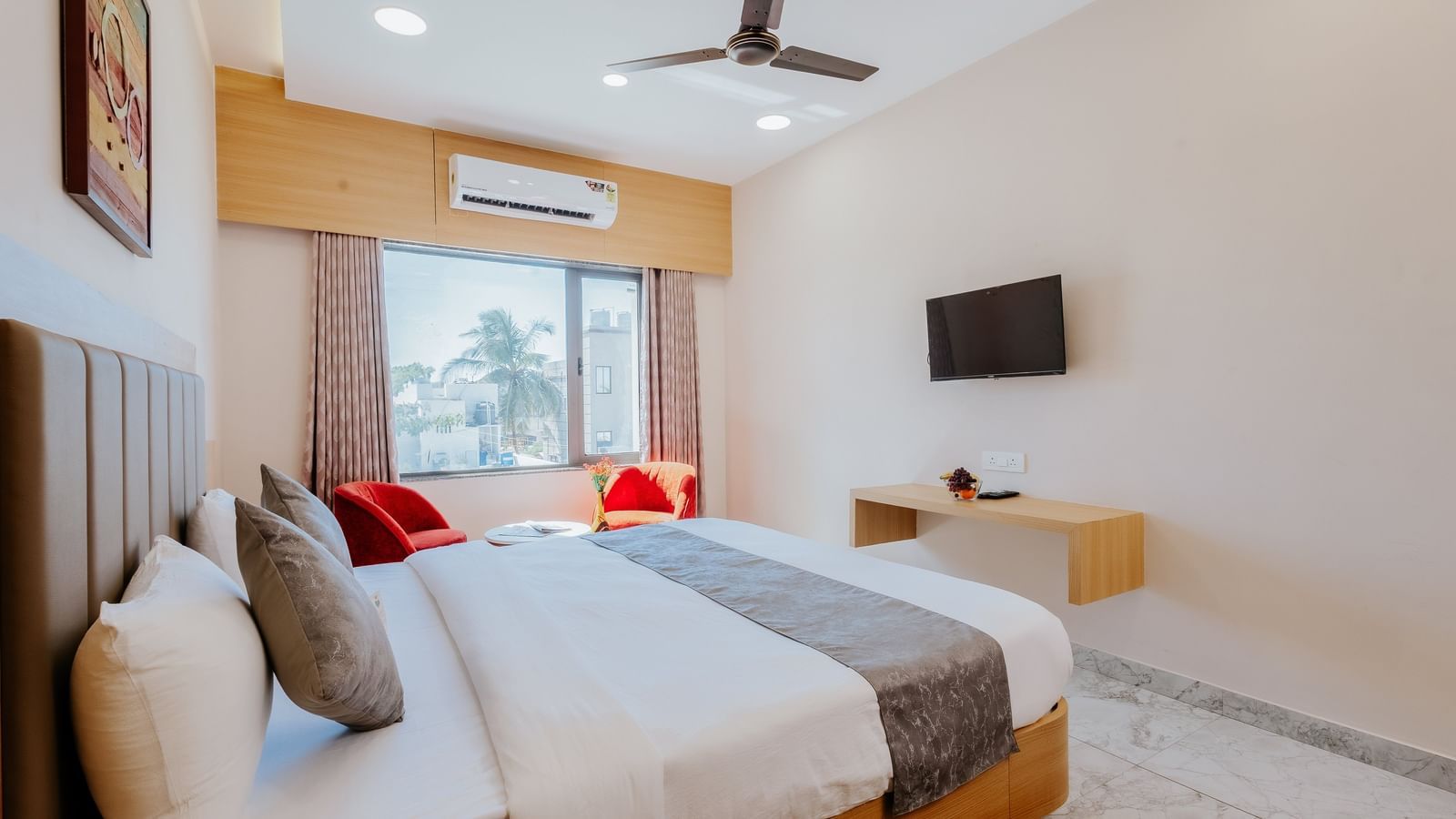 A spacious bedroom at Daksh The Grand Gowardhan, Dwarka, featuring a double bed placed opposite to a wall mounted television, and a window offering natural light.