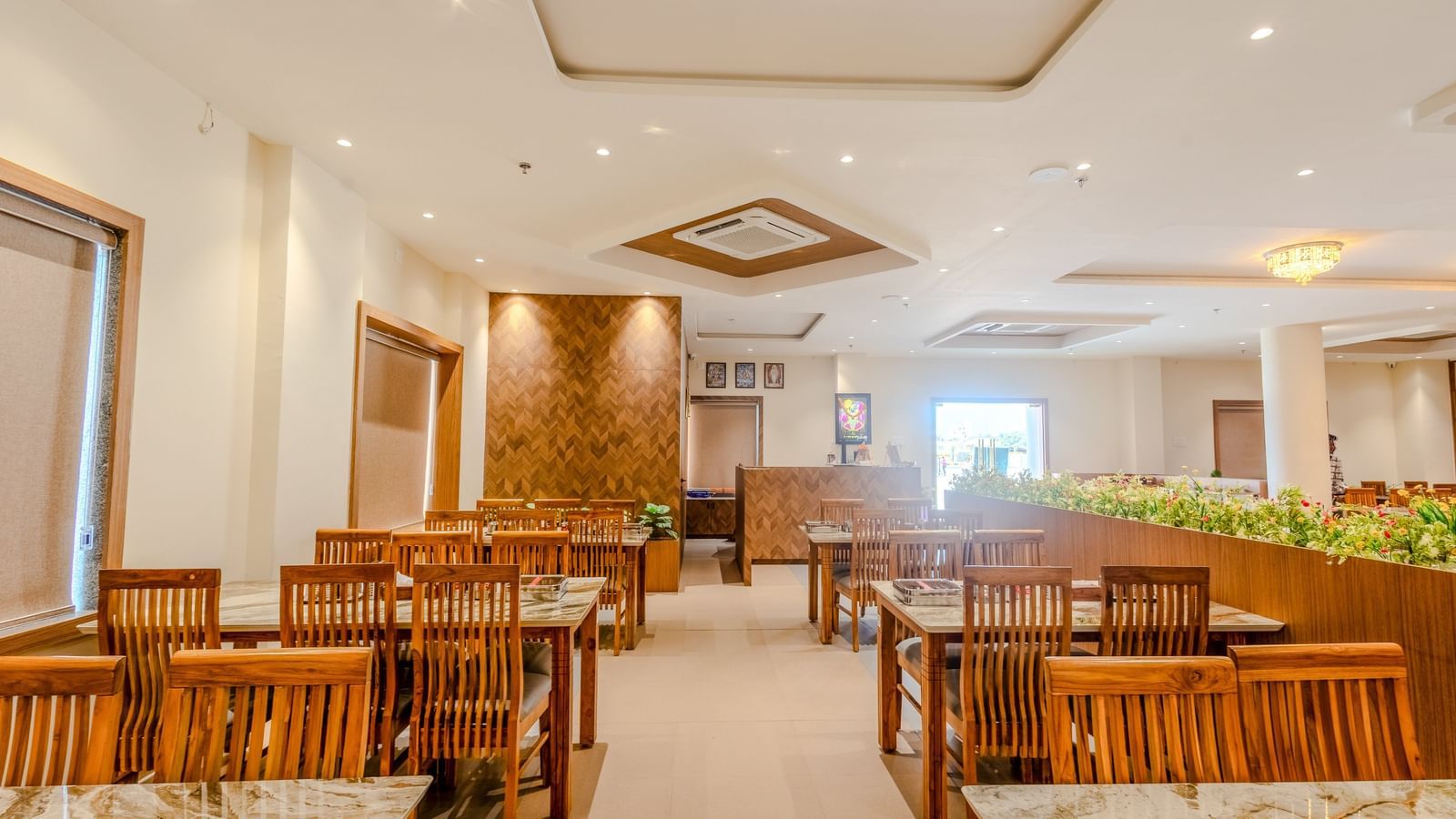 Interior of the dining area at Daksh The Grand Gowardhan, Dwarka, featuring wooden tables and chairs, with warm lighting.