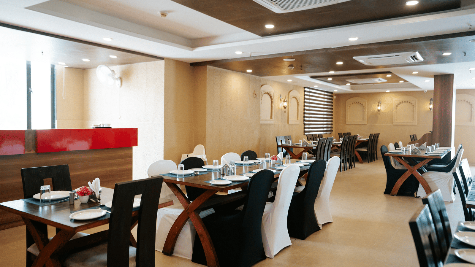 Detail of a restaurant table setting with a blue runner, plates, and dark chairs set against a textured wall with arches at Daksh The Madhuvan Suites, Dwarka.