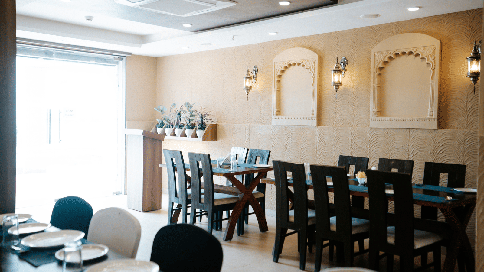 View across the set dining tables towards the buffet area, with warm lighting and a dark ceiling feature at Daksh The Madhuvan Suites, Dwarka.