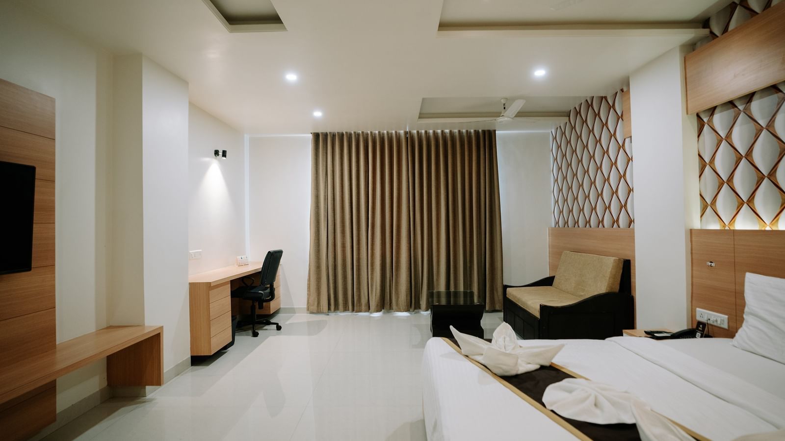 Wide angle view of the modern room showing the double bed, a small sofa, patterned curtains, and the general room layout at Daksh The Madhuvan Suites, Dwarka.