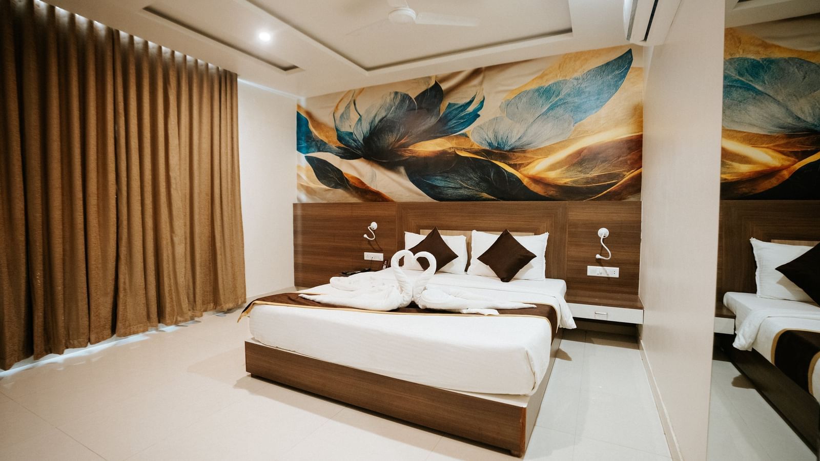 Double bed with dark brown frame and runner. The wall features a large, colourful, abstract floral painting above the wooden headboard at Daksh The Madhuvan Suites, Dwarka.