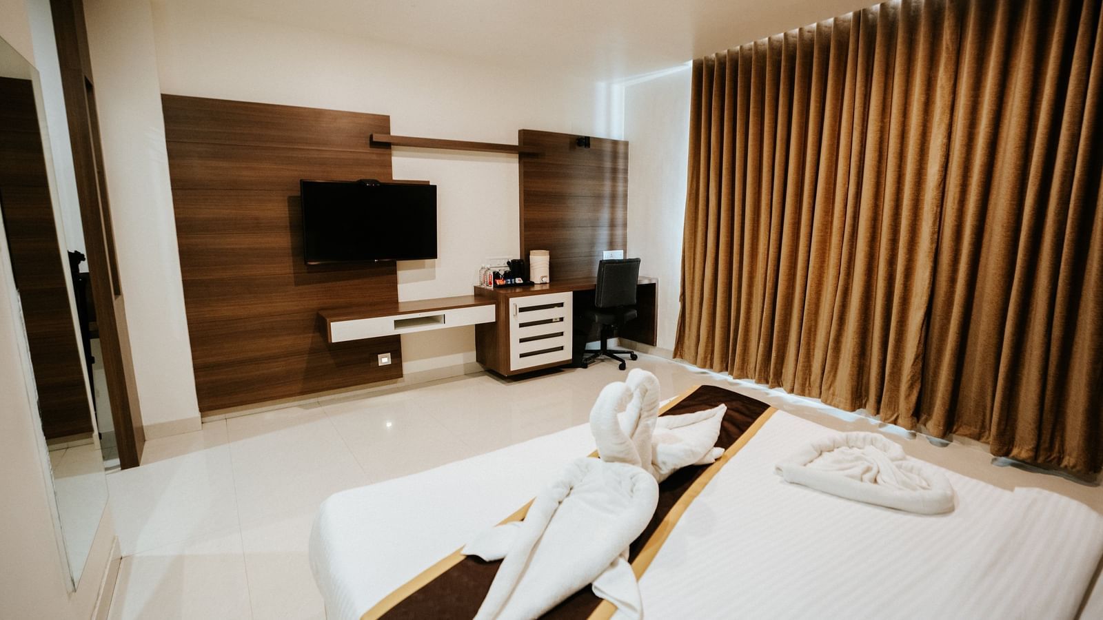 Spacious hotel room featuring a large, abstract floral painting above the bed, modern dark wood fittings, and white tiled floor at Daksh The Madhuvan Suites, Dwarka.