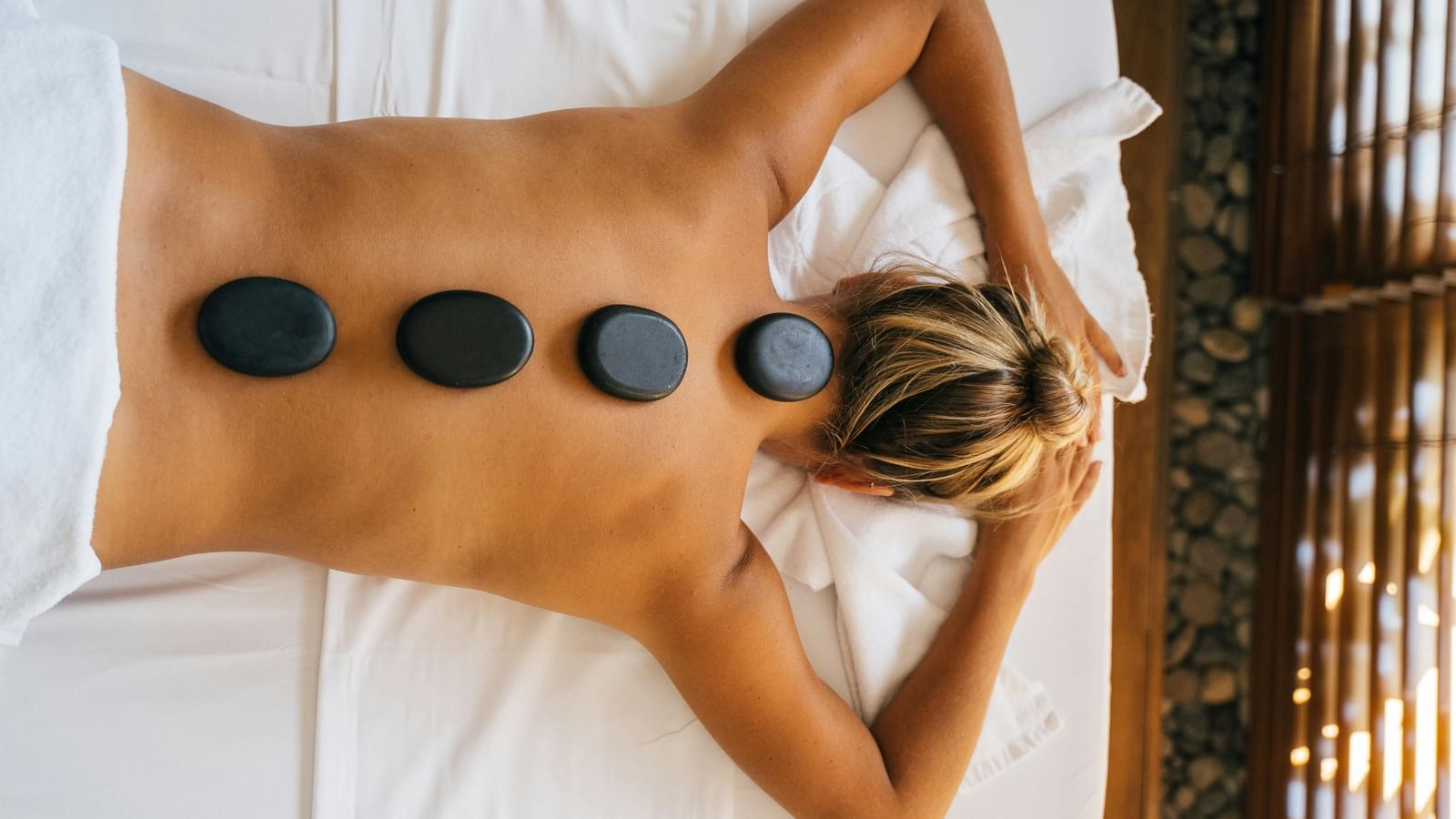 A woman lying down with back with black stones kept over her spine. (1)