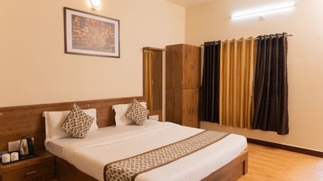 A neatly arranged double bed with patterned cushions and curtains at Daksh Resort & Amusement Park, Sasan Gir.