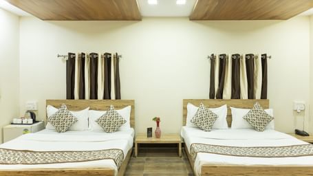 A guest room with two double beds, brown and white curtains, and ceiling lights at Daksh Resort & Amusement Park.