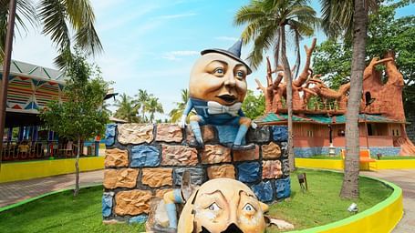 An artistic sculpture of humpty dumpty garden at MGM Dizzee World showcasing large, carved stone faces with vibrant surroundings and tropical trees.