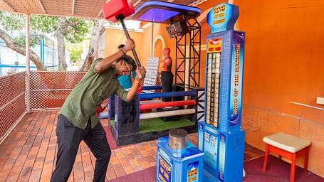 Visitor playing a high striker hammer game at MGM Dizzee World, preparing to hit with a large red mallet in a vibrant arcade setting.