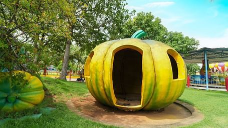 A whimsical, oversized pumpkin playhouse for children to explore at MGM Dizzee World, set in a green open space with palm trees.