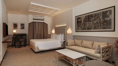 Executive Queen at Shilton Suites, Bengaluru, featuring a king size bed, sofa seating, coffee table, work desk, wardrobe and framed wall artwork.