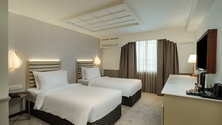 Executive Twin Room at Shilton Suites, Bengaluru, featuring twin beds, bedside tables, floor lamps, work desk and curtains. 