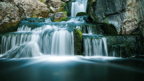 An overview of a Waterfall cascading down to a waterbody with boulders surrounding it