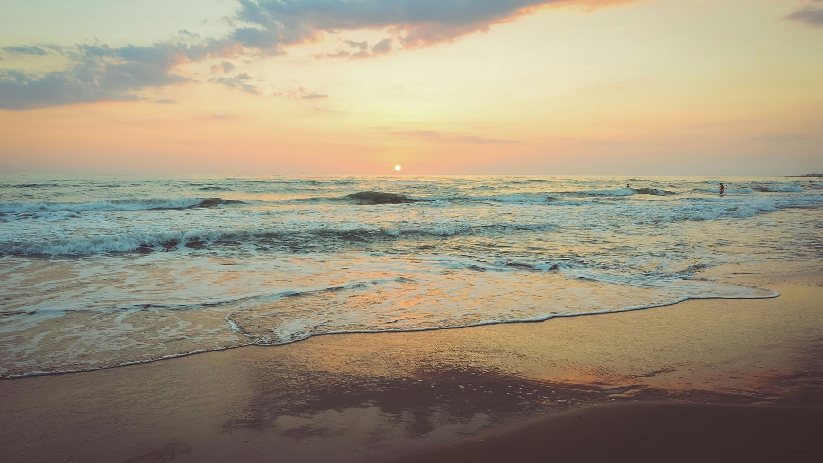 Serene sunset over a sandy beach with gentle waves.