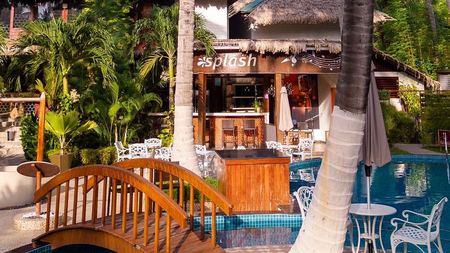 A view of a beautiful pool area with comfortable lounge chairs, palm trees, and a lush garden surrounding the pool. The atmosphere is calm and inviting, ideal for relaxation - Coral Reef Resort & Spa, Havelock
