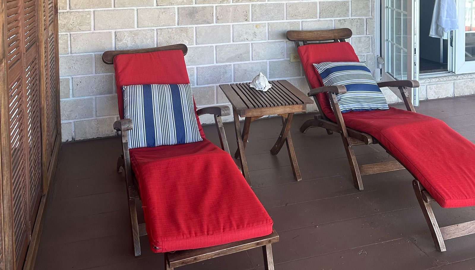 Covered porch with red lounge chairs and small tables outside a room | A Stone's Throw Away