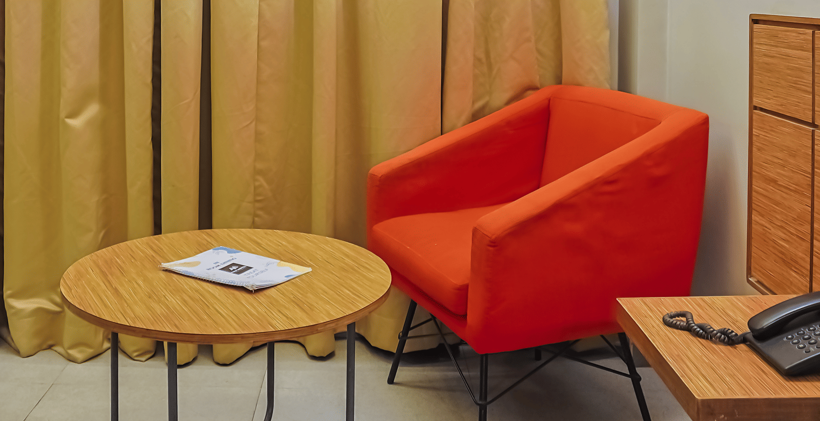 Seating corner with orange chair, round table and curtains at Max Hotel Prayagraj.